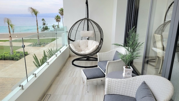 Un balcón con mobiliario de mimbre, una silla colgante y vistas al océano.