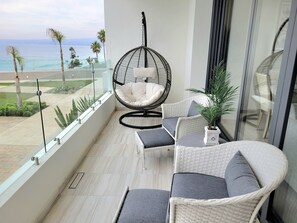 A balcony with wicker furniture, a hanging chair, and a view of the ocean. - Seafront Luxury Condo Pool Jacuzzi (Playas de Rosarito)