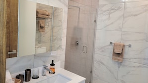 Un baño moderno con un lavabo blanco, cabina de ducha con paredes de cristal y paredes de mármol.