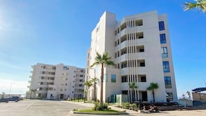 Un moderno edificio de varios pisos con balcones, zona de estacionamiento y palmeras.