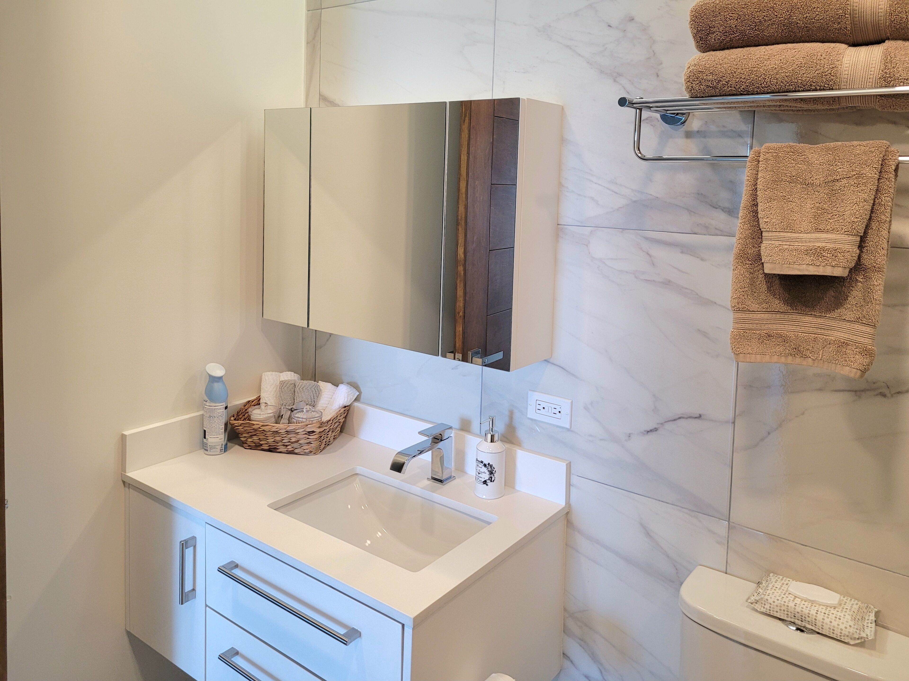 Une salle de bain moderne avec un meuble-lavabo blanc, un grand miroir, un porte-serviettes avec des serviettes et des toilettes.