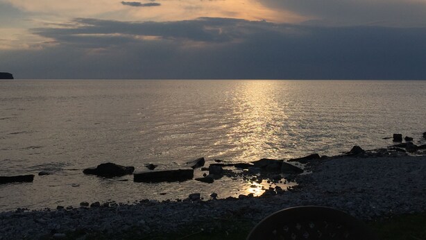 Tramonto sul mare calmo con una costa rocciosa.