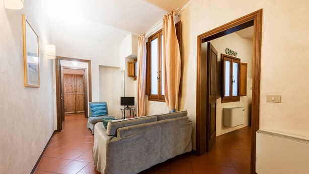 Un couloir avec un canapé, une lampe, un téléviseur et une porte portant l’inscription « COSTA ».