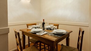 Une table à manger dressée avec des assiettes, des verres et des couverts, une bouteille de vin et un luminaire fixé au mur.
