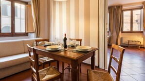 Un comedor con una mesa de madera dispuesta para cuatro personas, un sofá y una ventana con cortinas.