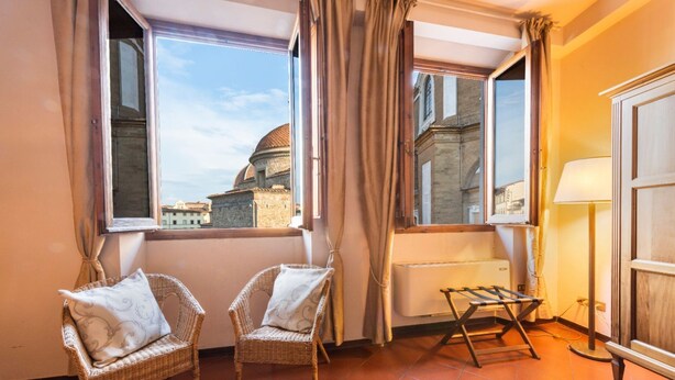 Una habitación con dos sillas de mimbre, un radiador, una ventana con cortinas y vistas a una cúpula y edificios.