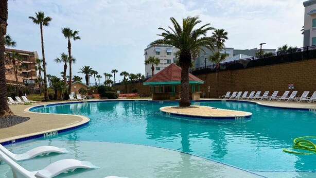 Una piscina con sillas de descanso, palmeras y un pequeño pabellón.