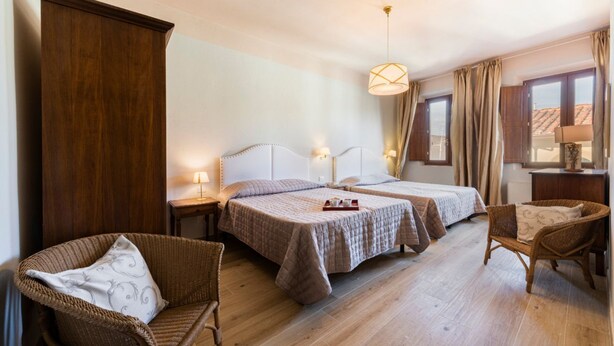 Ein Hotelzimmer mit zwei Betten, einem großen Holzschrank, Korbstühlen und einer Hängeleuchte.
