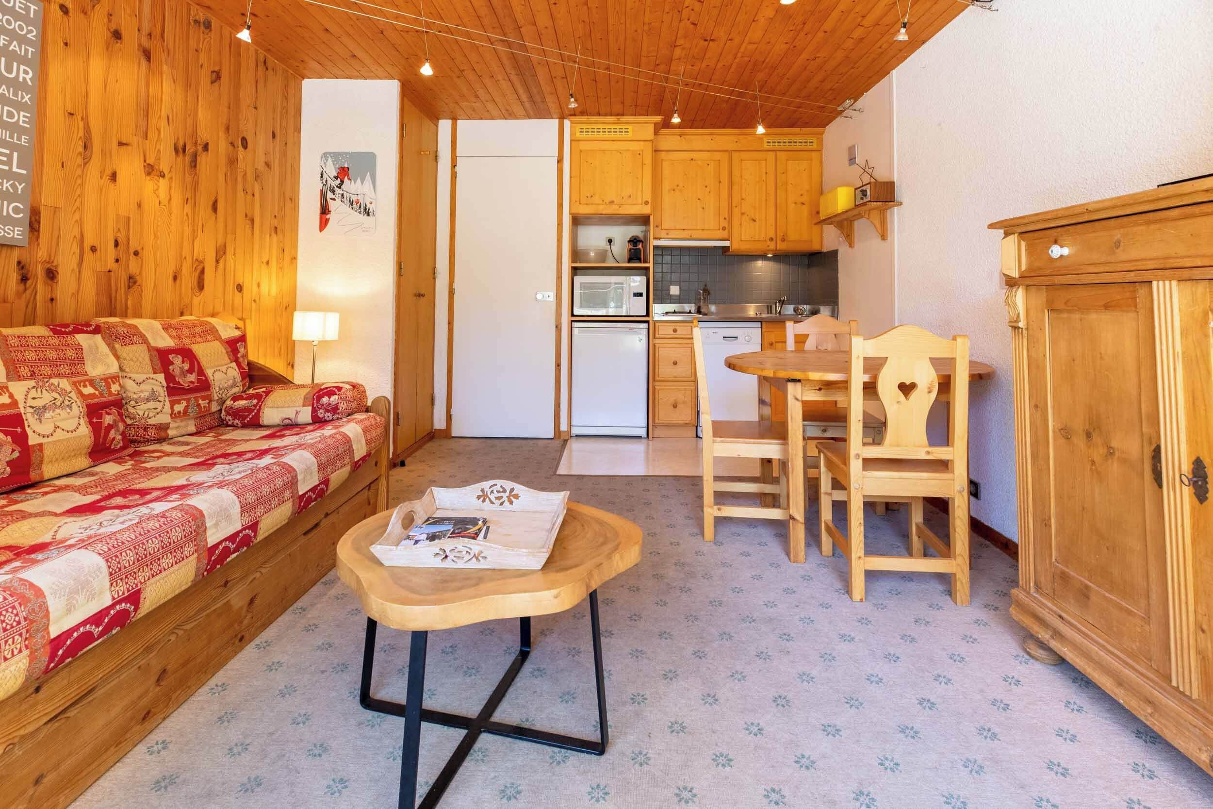 Ett mysigt rum med en soffa i trä, ett litet träbord, en köksdel med träskåp och ett kylskåp.