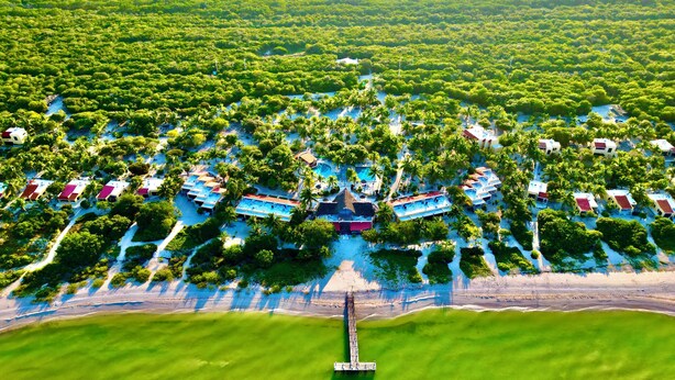 Une vue aérienne d’un complexe hôtelier comprenant plusieurs hébergements de type bungalow, disposés autour d’une piscine centrale et reliés par des allées.