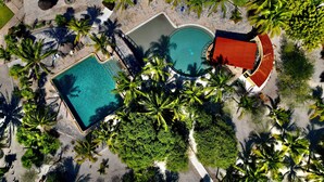 Vue aérienne d’un complexe hôtelier doté de deux piscines, de palmiers et d’un bâtiment au toit rouge.