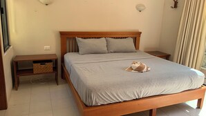 Un lit bien fait, recouvert d’une couvre-lit grise et agrémenté de deux oreillers, une table de chevet en bois avec un panier en osier, un luminaire fixé au mur et un rideau à la fenêtre.