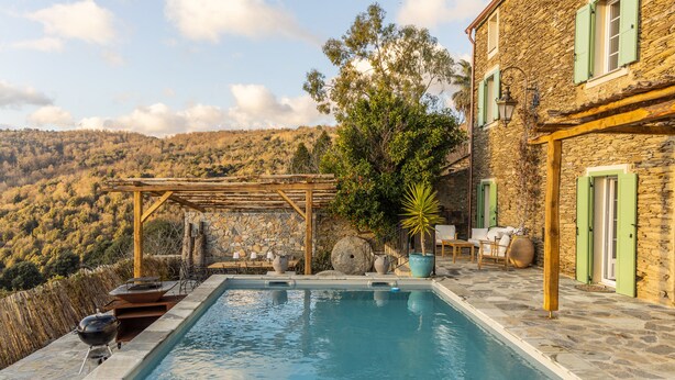 A stone pool with a pergola, outdoor seating, and a view of a hillside.