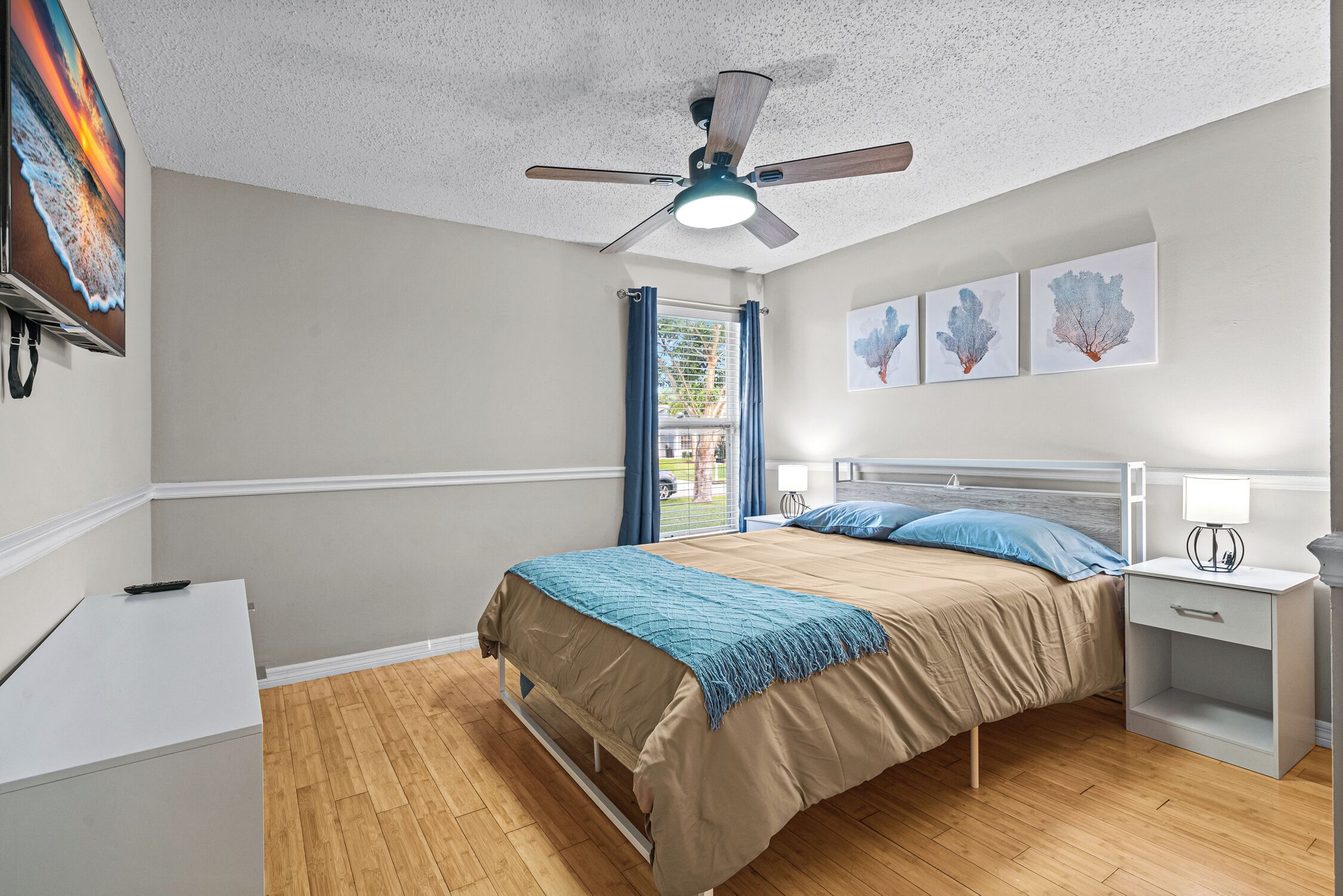 A bedroom with a bed, nightstands, a ceiling fan, and artwork on the wall.