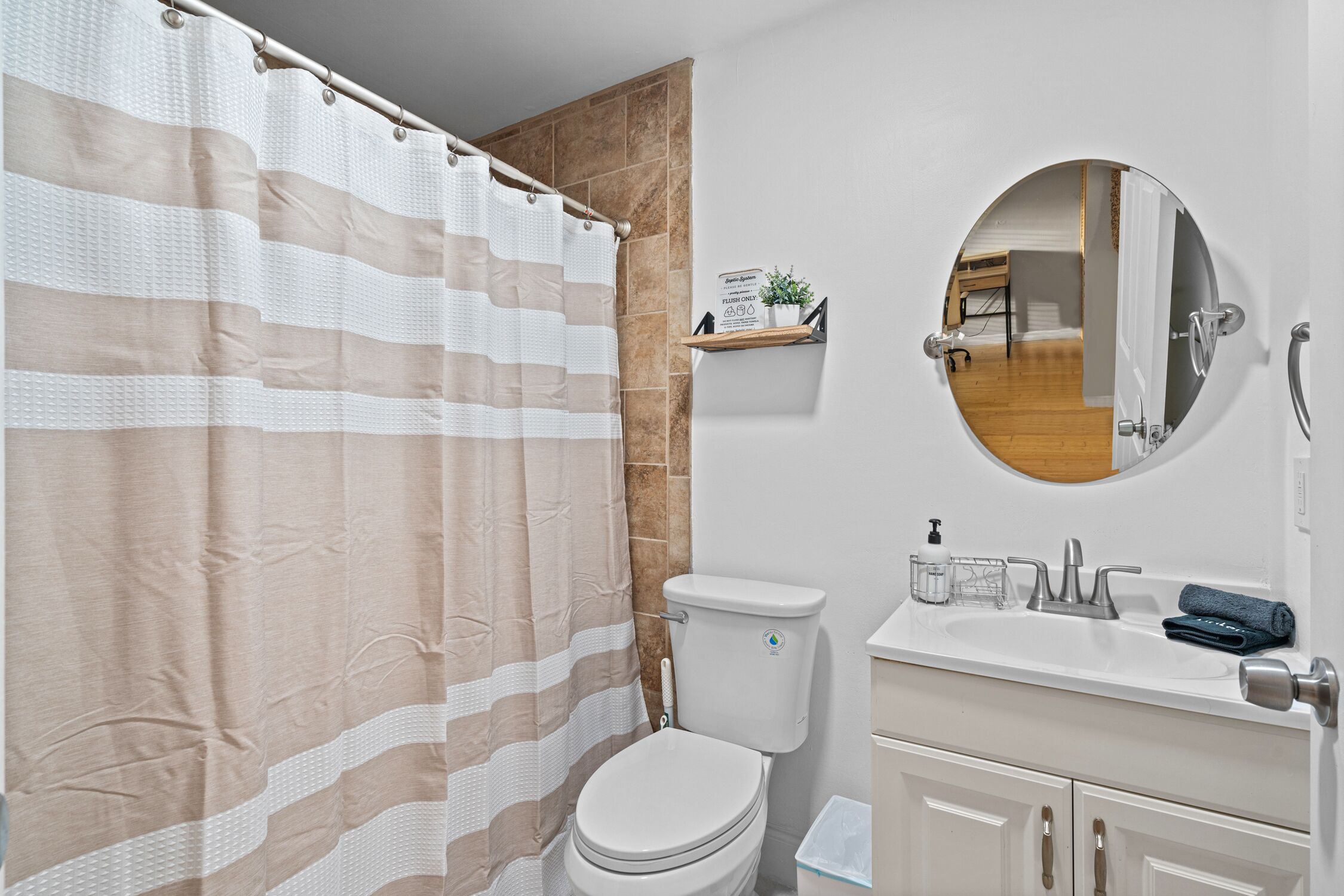 A bathroom with a striped shower curtain, a toilet, a sink with a mirror, and a small shelf with toiletries.