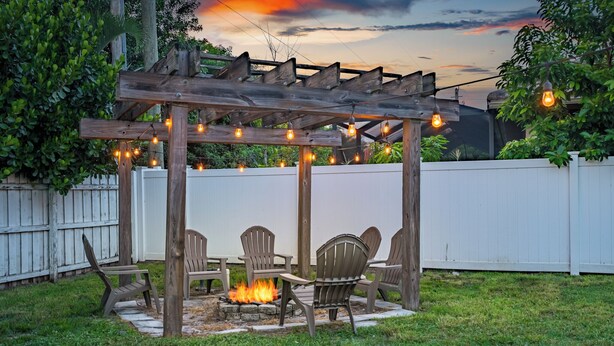 Una pérgola de madera con luces colgantes, un brasero y asientos al aire libre.
