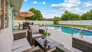 Un patio al aire libre con mobiliario de mimbre, piscina y vistas al jardín.