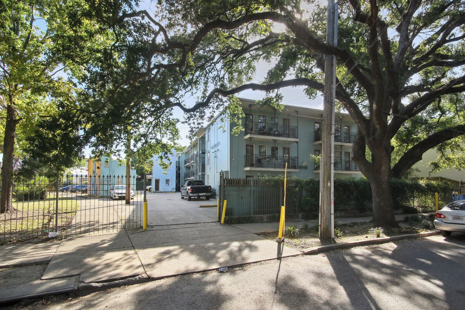 A residential building with a gated entrance, a parking area, and a large tree in the foreground.