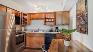 A modern kitchen with wooden cabinets, stainless steel appliances, and a dining area with a wooden table and potted plant.