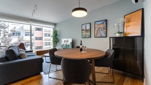 Ein modernes Wohnzimmer mit einem runden Holztisch, grauen Sofas und einem großen Fenster mit Blick auf die Stadt.
