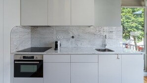 Eine moderne Küche mit weißen Schränken, einer Marmorarbeitsplatte, einem eingebauten Backofen, einer Kaffeemaschine und einem Fenster mit Blick auf Bäume.