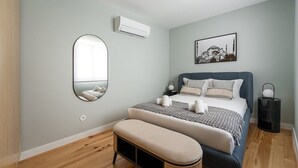 Ein Schlafzimmer mit einem Bett, einem Nachttisch, einer Lampe, einem Spiegel und einer Wand-Klimaanlage.
