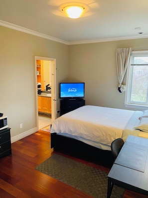 A bedroom with a bed, a desk, a television, and a bathroom visible through an open door.