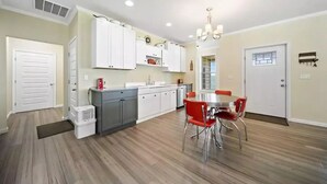 A modern kitchen with white cabinets, a grey countertop, and a dining area with red chairs.