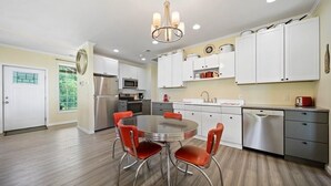 A modern kitchen with stainless steel appliances, white cabinets, and a round dining table with red chairs.