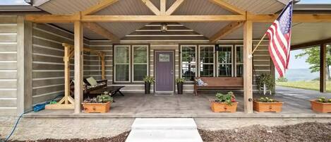 A covered porch with a wooden bench, potted plants, and an American flag.