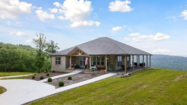 A two-story log cabin with a covered porch and a view of the surrounding landscape.