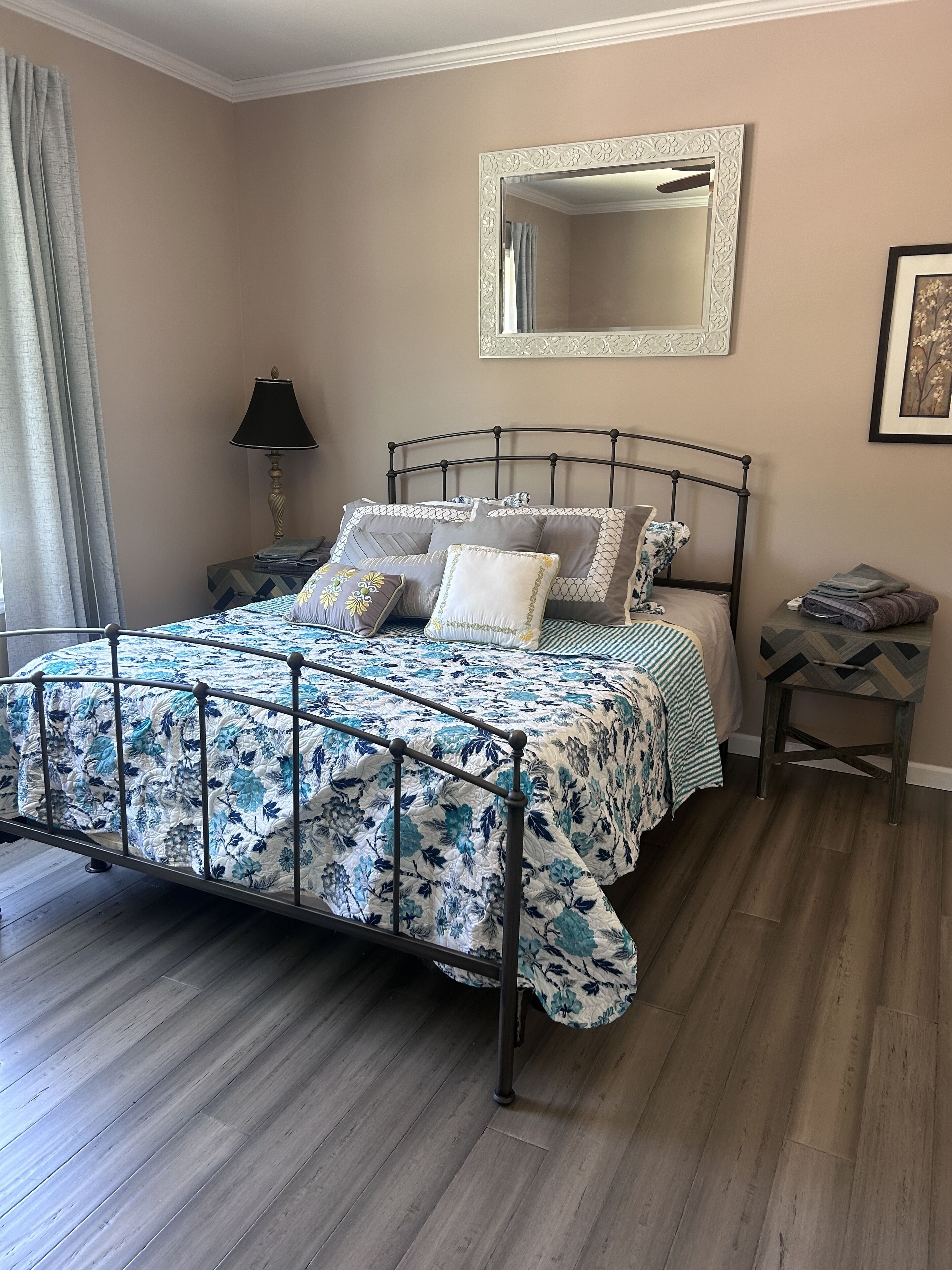 A neatly made bed with a floral bedspread, a bedside lamp, and a mirror on the wall.