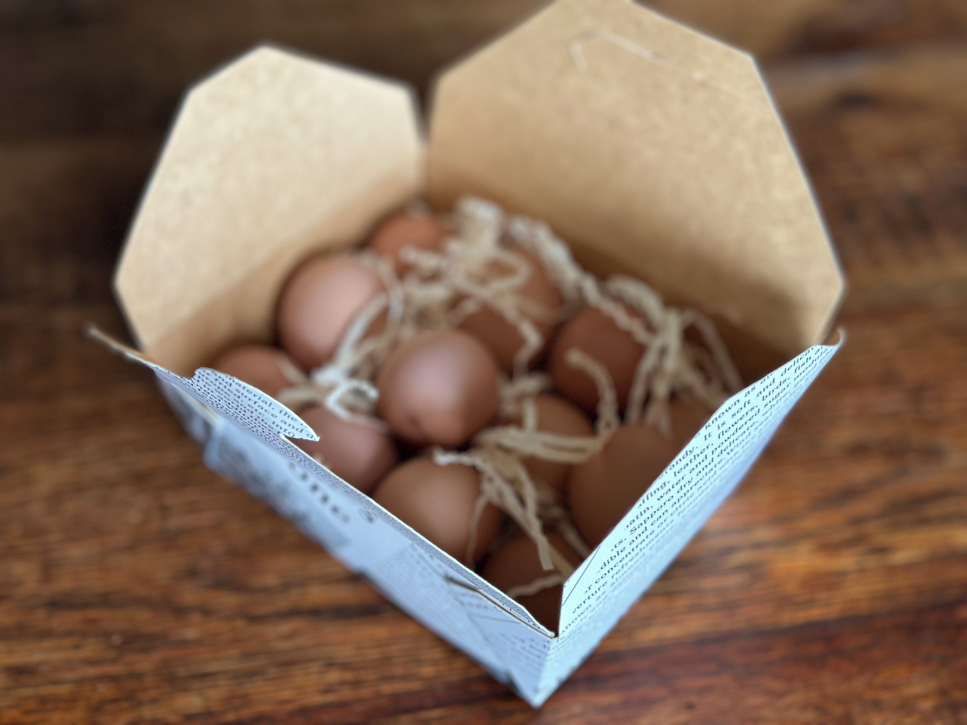 A cardboard box containing brown eggs with straw.