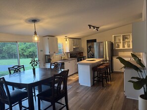 A modern kitchen with white cabinetry, a central island, and a dining area with dark chairs.