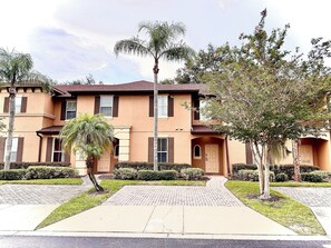 Stucco and brick building with a flat roof, central entrance, and manicured lawns.