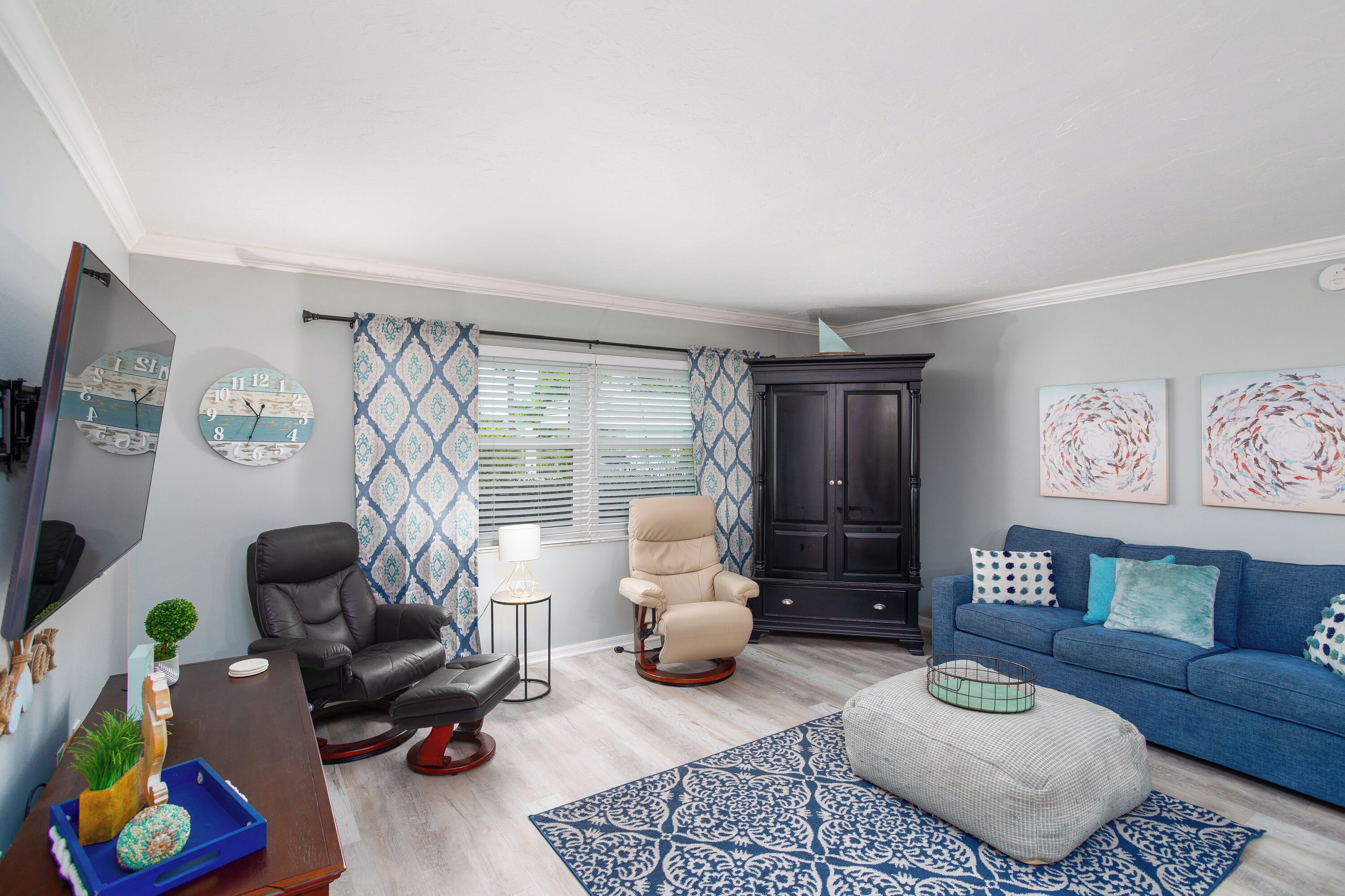 Een woonkamer met een zwarte leren fauteuil, een blauwe bank en een zwarte kast.