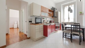 A modern kitchen with a microwave, oven, and red cabinets. There is a dining table with chairs and a window with curtains.