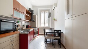 A compact kitchen with a microwave, stove, and red cabinetry. There is a dining table with chairs and a window with curtains.