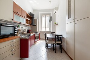 Cozinha compacta com micro-ondas, fogão e armários vermelhos. Há uma mesa de jantar com cadeiras e uma janela com cortinas.
