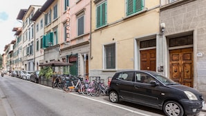 A street with parked cars and bicycles, buildings with shutters, and a sign for 'DOTTORI'.