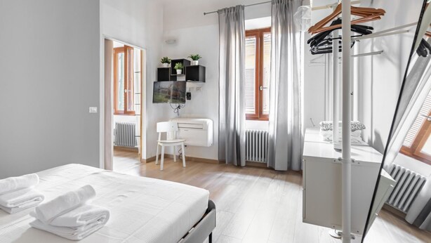 A modern hotel room with a bed, a chair, a radiator, a TV, and a wardrobe.