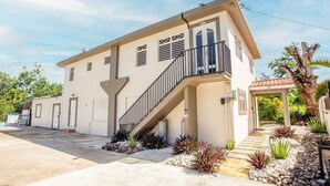 A two-story building with a staircase leading to a balcony, surrounded by landscaped garden beds and a palm tree. - EcoMar Rentals #1: Cabo Rojo, Puerto Rico; Beach & Pool (Cabo Rojo)