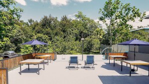 An outdoor patio with wooden tables and chairs, two blue umbrellas, and a barbecue grill. - EcoMar Rentals #1: Cabo Rojo, Puerto Rico; Beach & Pool (Cabo Rojo)