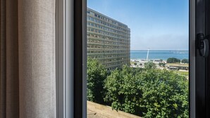 Vista desde una ventana con cortina, que da a un edificio grande, un puente y una masa de agua.