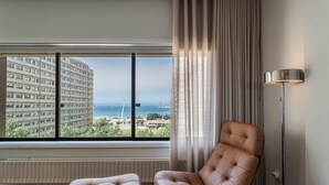 Una habitación con un ventanal grande, un sillón de cuero, una lámpara de pie y un radiador.