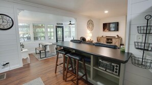 A modern kitchen with a central island, bar stools, a clock, and a television.