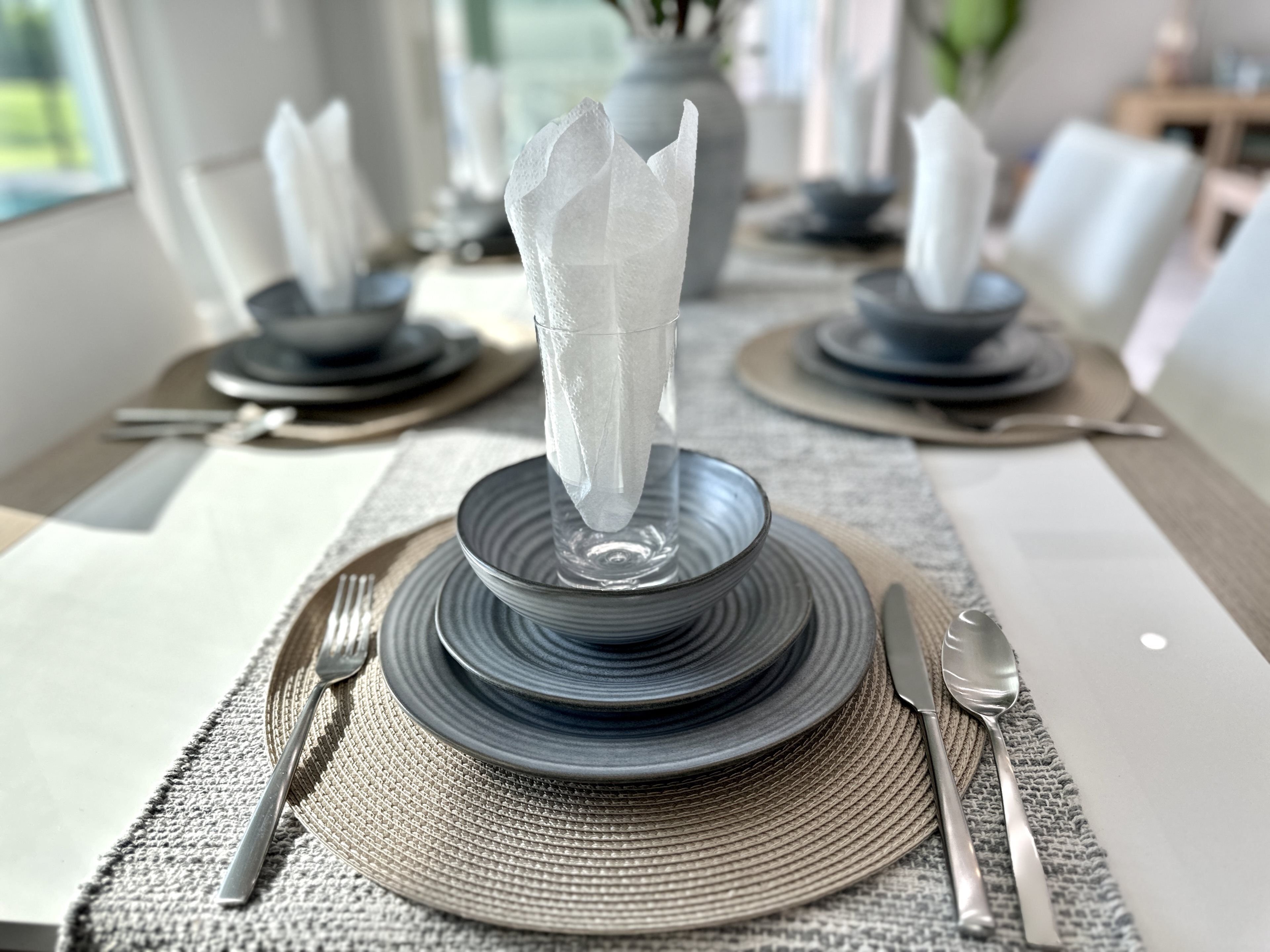 Una mesa de comedor dispuesta con platos, cubiertos y servilletas.