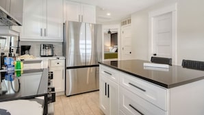 A modern kitchen with white cabinets, a stainless steel refrigerator, and a black countertop. - 200 steps to the Beach | Heated pool + spa (Holmes Beach)