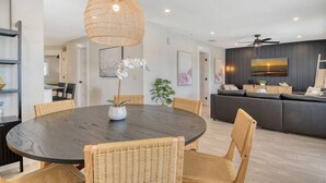 A modern dining area with a round table, wicker chairs, and a hanging light fixture. - 200 steps to the Beach | Heated pool + spa (Holmes Beach)