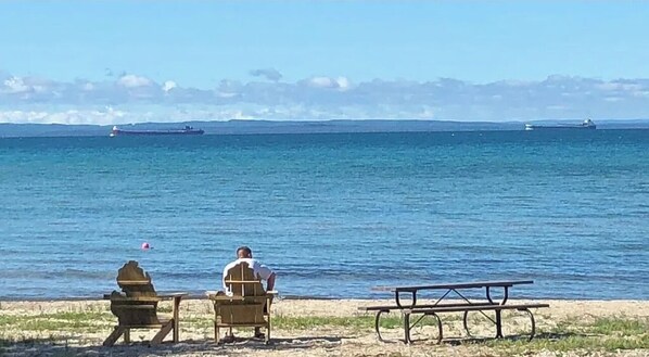 Relax on the beach with a clear ocean view, a picnic table, and two chairs.